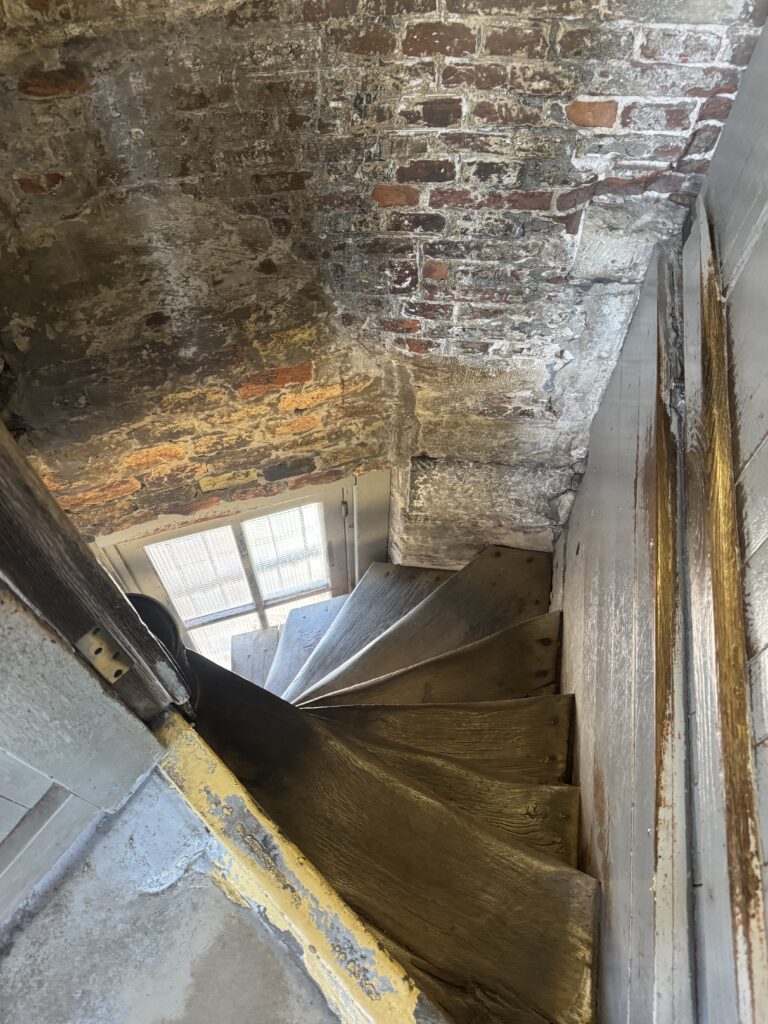 A spiral staircase inside a building, featuring a textured brick wall in the background.